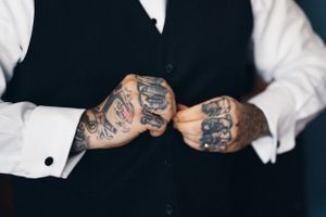Close-up of tattooed hands adjusting formal wear cuffs.