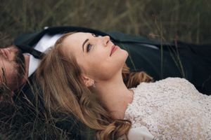 A bride lies back in lace dress amid nature during outdoor photo session.