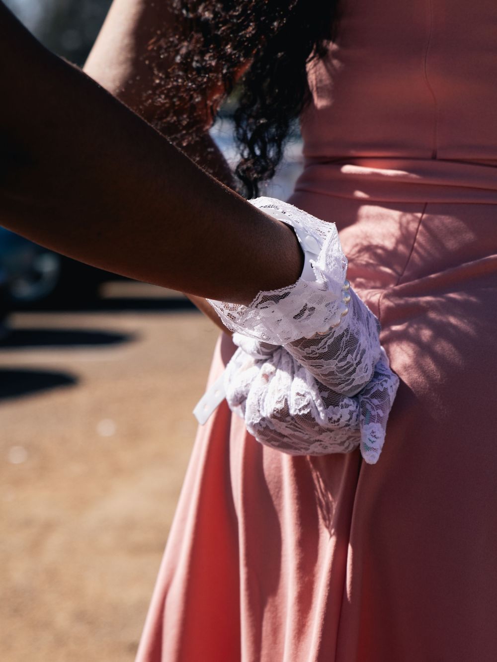 Close-up of hands wearing white lace gloves against pink fabric background.