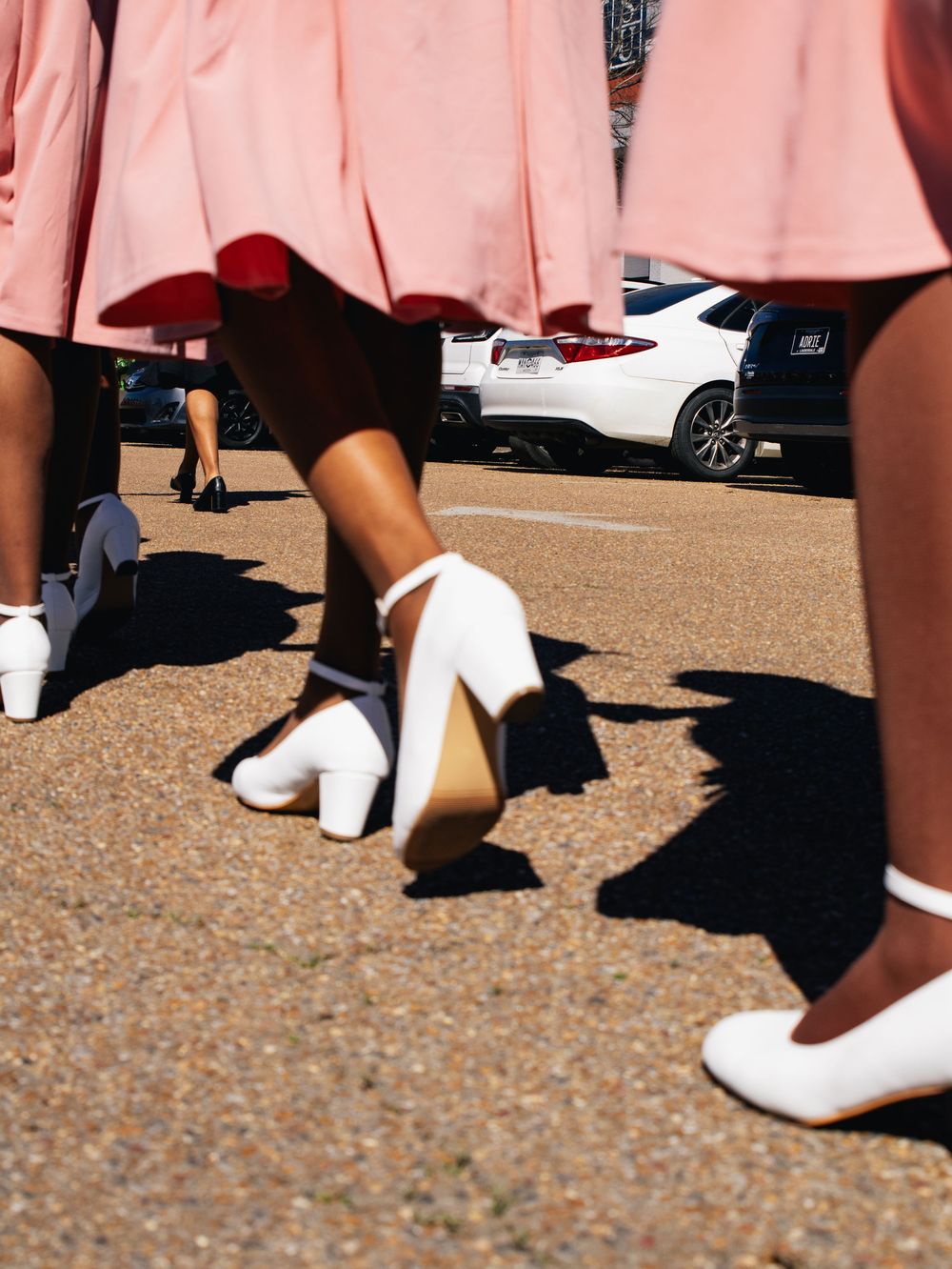 Detail shot of white shoes and pink dresses in an organized outdoor lineup.