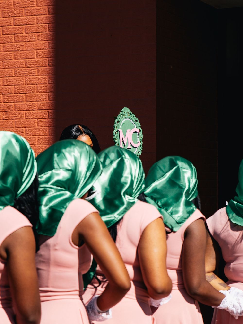 Artistic composition showing row of pink dresses against brick wall with green accessories.