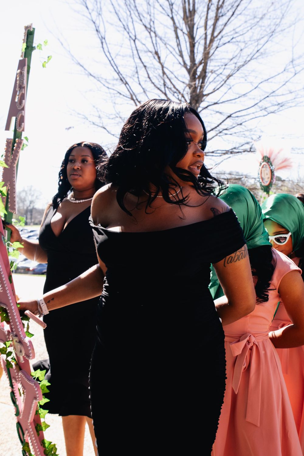 A gathering of people in formal attire including black dresses and pink gowns stand together outside.
