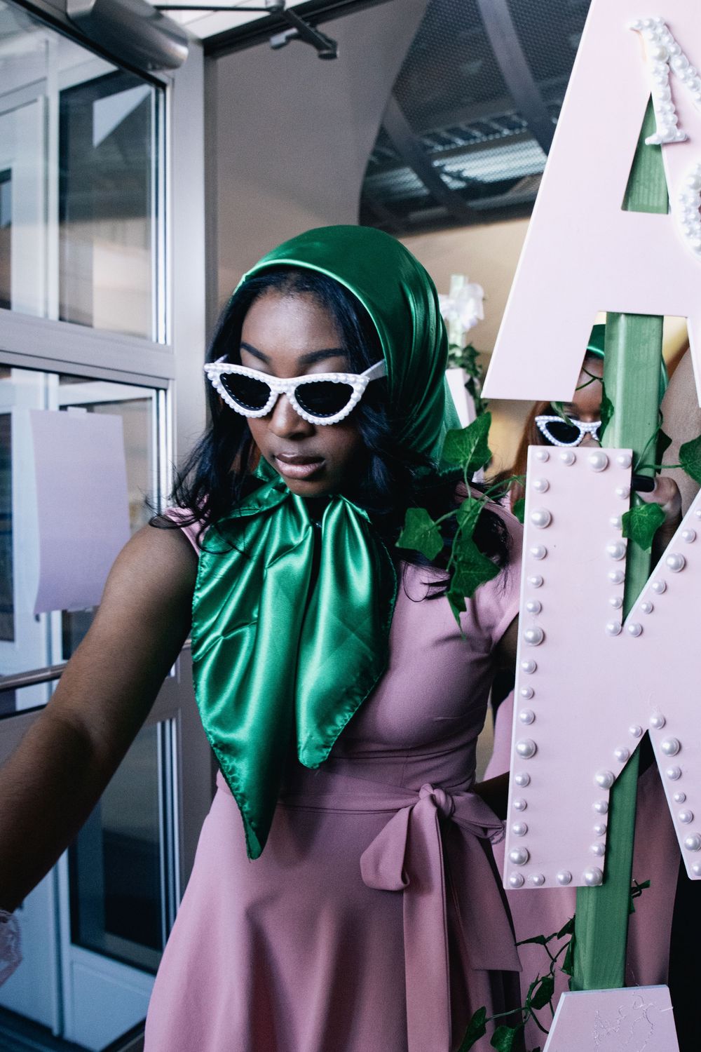 Fashion model wearing retro white sunglasses, pink dress and emerald green head scarf in stylized portrait series.