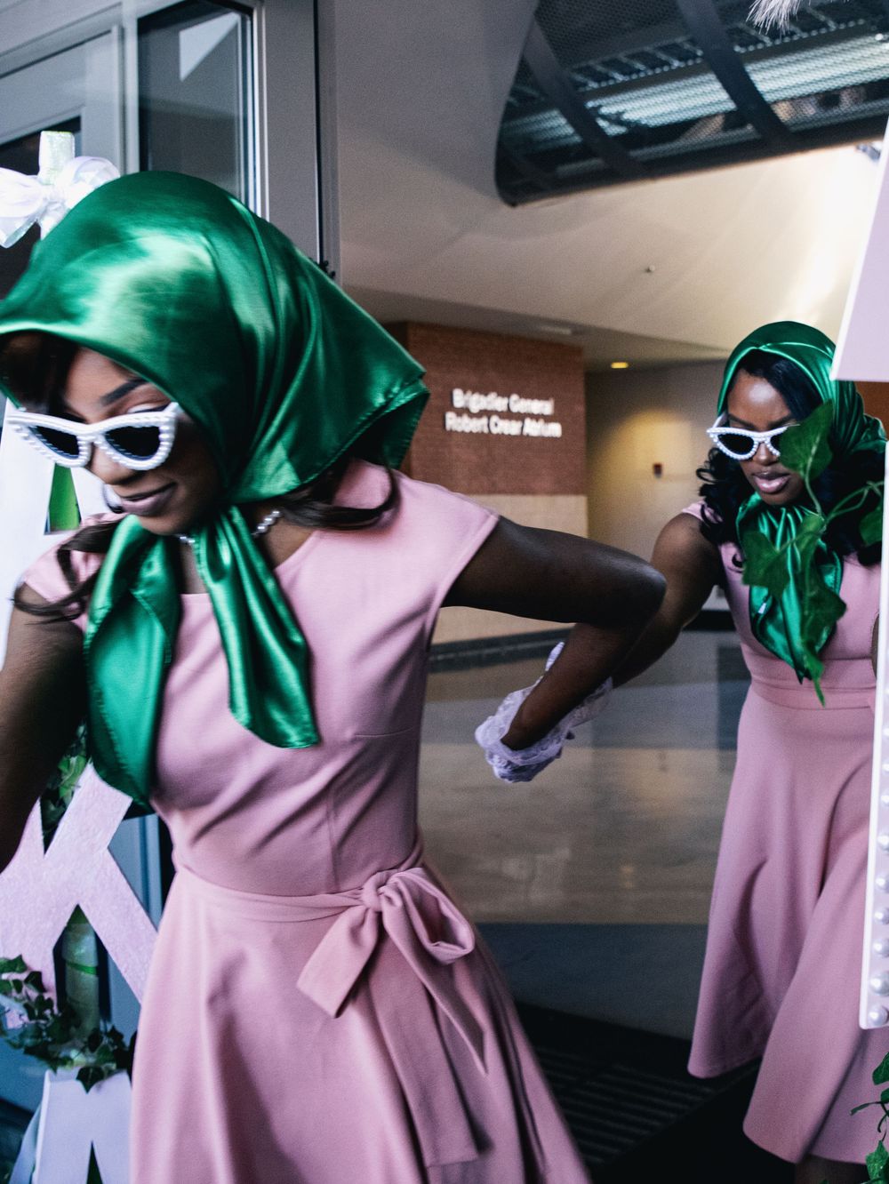 Fashion editorial featuring pink dress and green accessories against modern interior backdrop.
