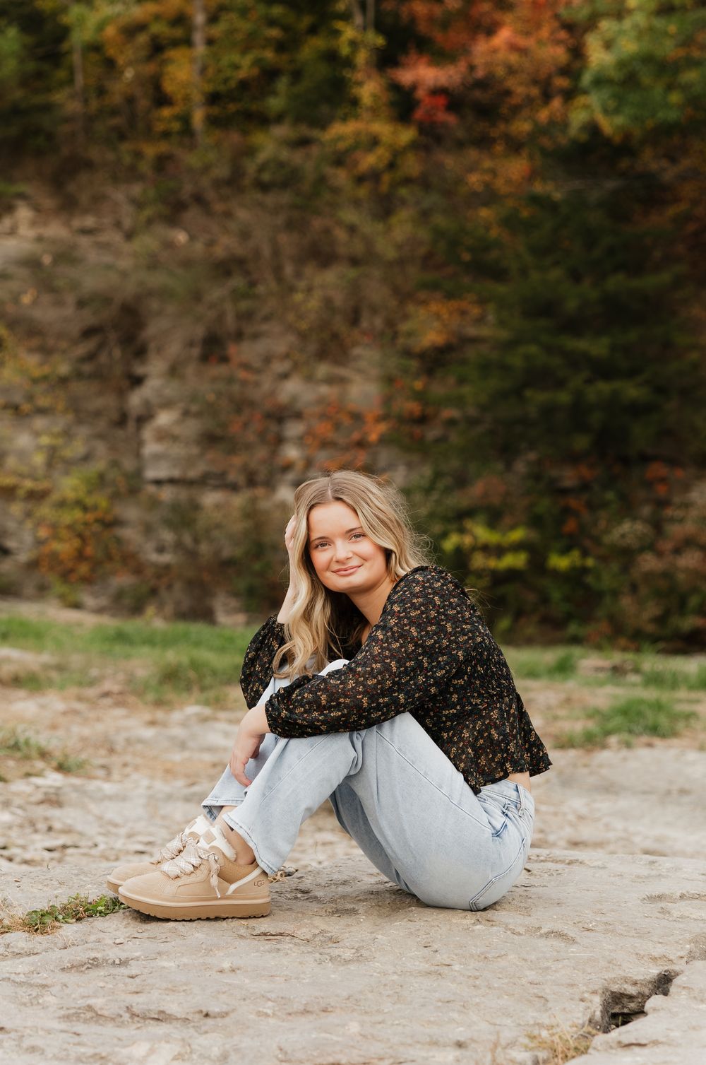 Person in a leopard print top and light jeans lounging on rocky ground surrounded by autumn foliage.