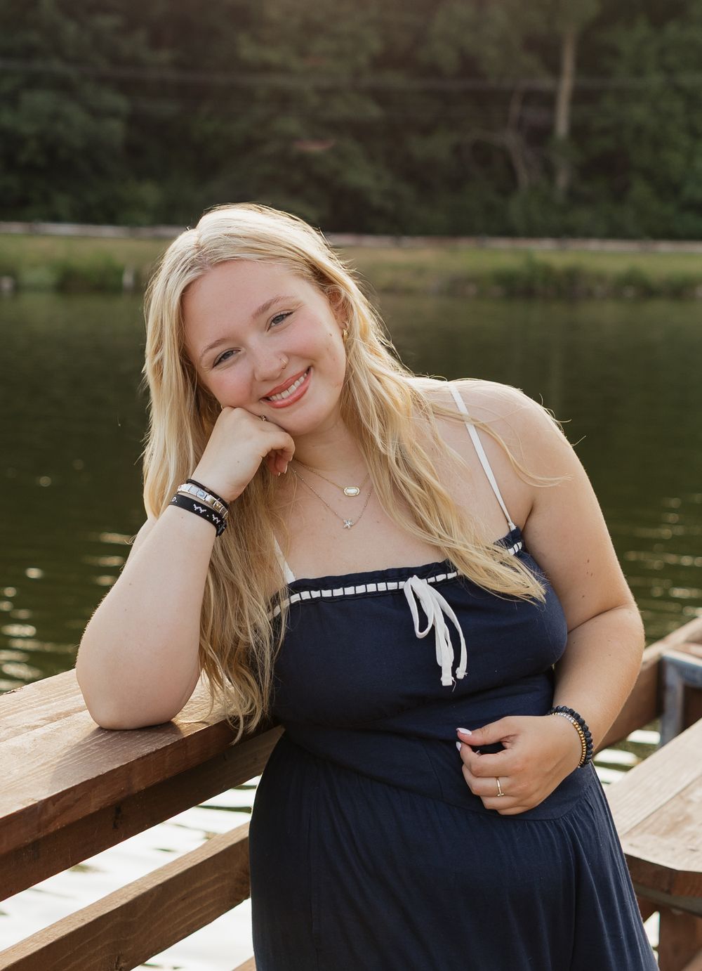 A series of outdoor portraits in a navy blue dress sitting on a wooden dock by a serene lake.