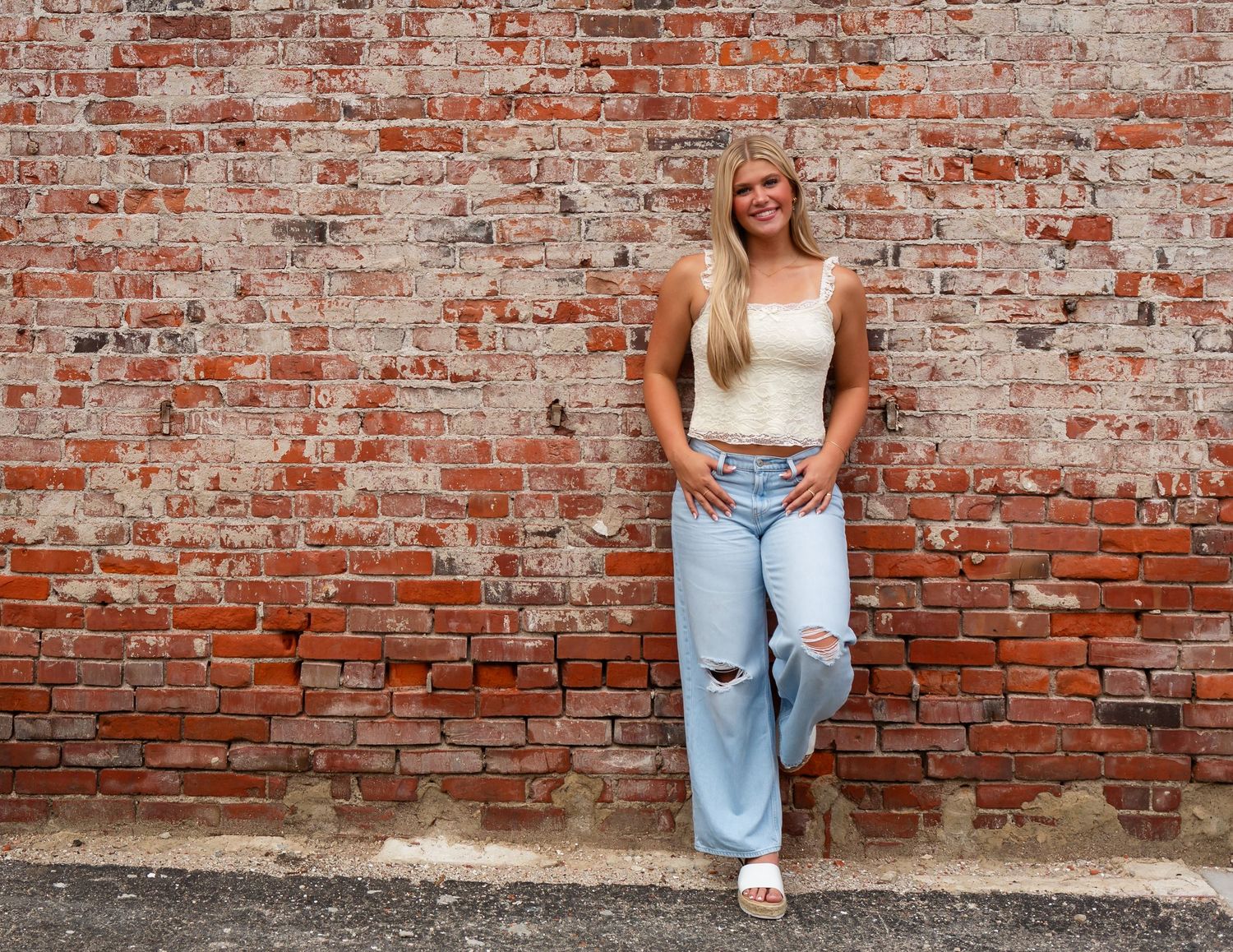 High school senior poses casually against a weathered brick wall in downtown Cedar Rapids.