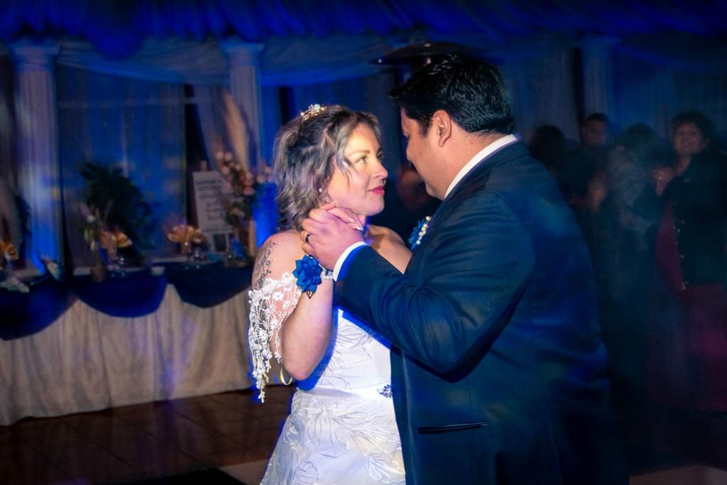 Pareja compartiendo su primer baile en la recepción de matrimonio con iluminación azul y decoración blanca.