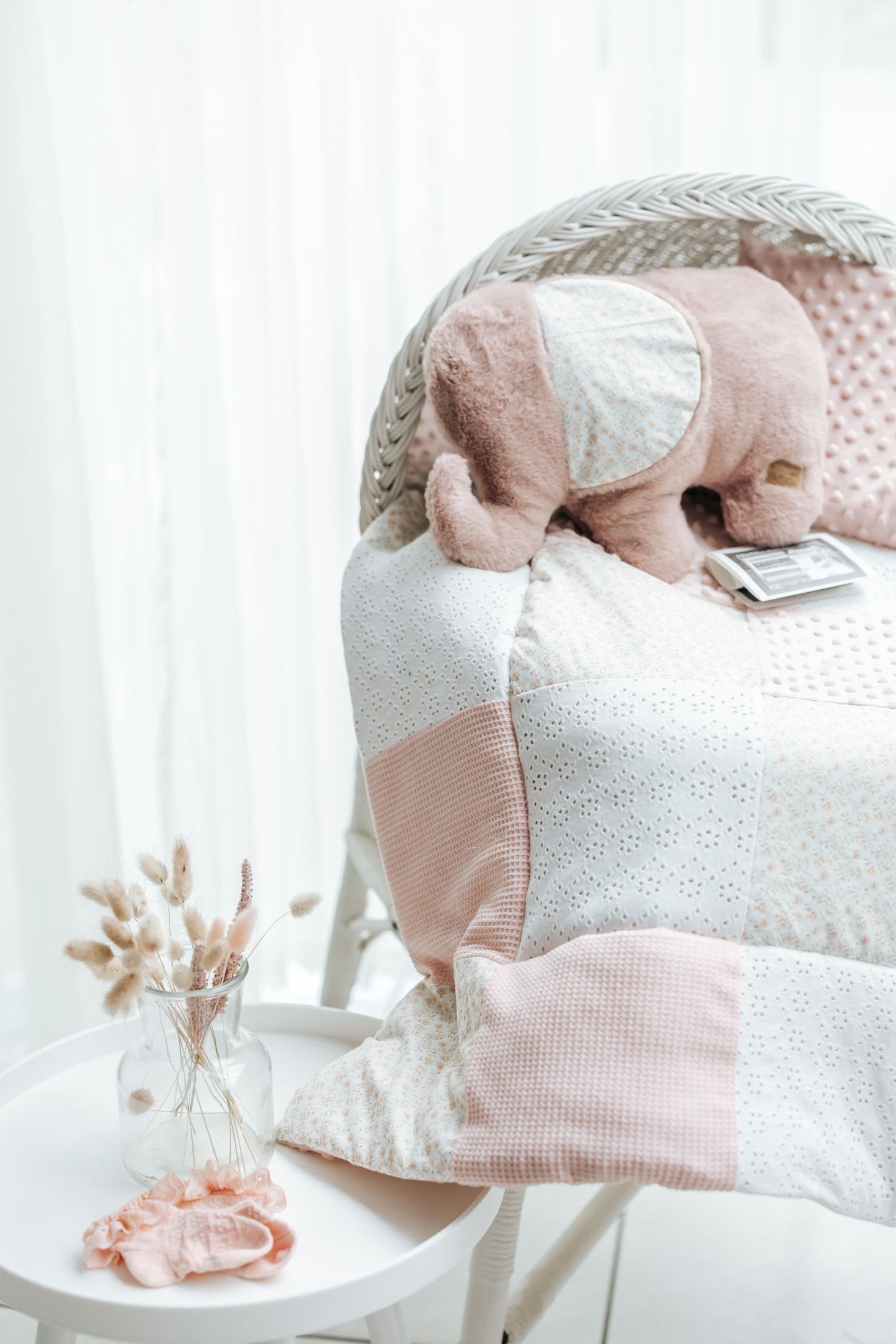 Soft pink and white nursery decor featuring a plush elephant toy and delicate textiles on a chair.