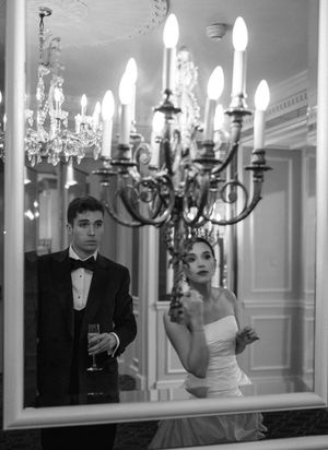 Dramatic black and white reflection of a couple in formal attire among elegant wall sconces and mirrors.