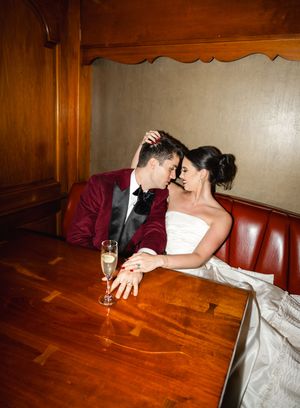 Wedding couple shares intimate moment on wooden floor with champagne glass nearby.