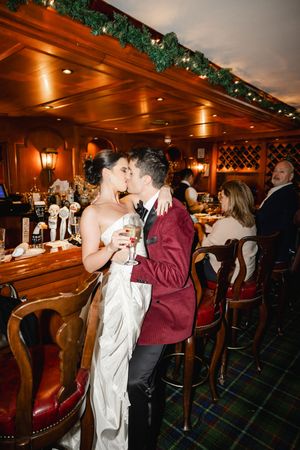 A couple shares a romantic moment at a bar decorated with greenery and warm lighting.