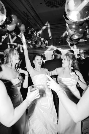 Wedding guests and bride dancing under silver balloons at a reception party.