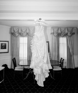 Black and white photograph showing a series of windows with billowing white curtains in an empty interior space.
