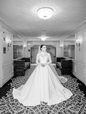 A bride poses in a grand ballroom wearing a stunning white ball gown with a full skirt.