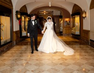 Wedding couple walks through an elegant marble hallway with arched ceilings.