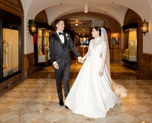 Wedding couple walking through an elegant marble hallway with arched ceilings and warm lighting.