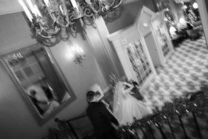 Black and white wedding dance photos under an elegant chandelier in a grand staircase setting.