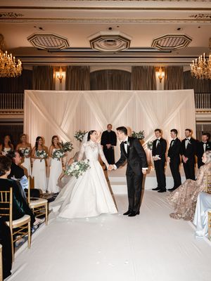 Elegant wedding ceremony setup in a grand ballroom with crystal chandeliers and white fabric backdrop.