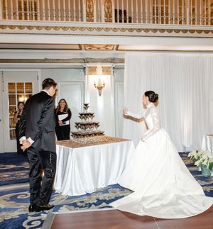 Wedding couple stands at opposite ends of an elegant tiered chocolate cake display at their reception.