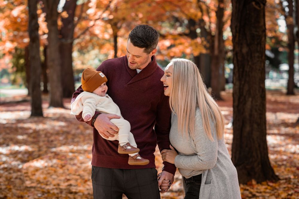 A family shares a joyful moment together in a park surrounded by autumn trees with orange fallen leaves.