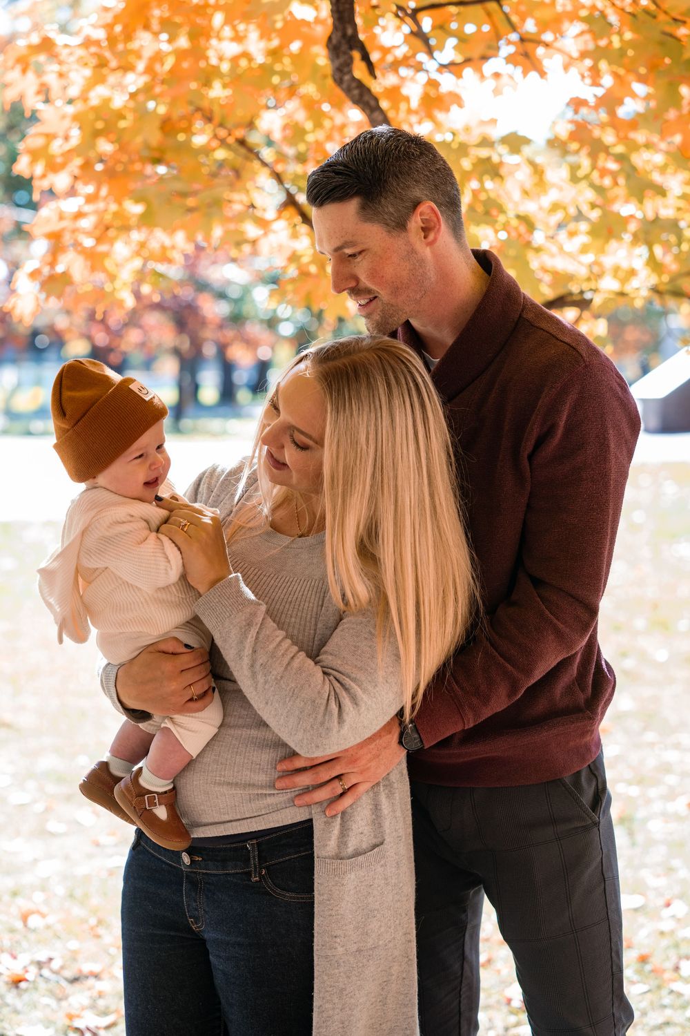 Family shares tender moments together during autumn photoshoot with golden fall foliage in background.