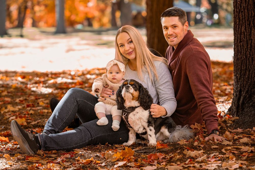 A couple and their dog lay on autumn leaves during a cozy fall photoshoot in the park.