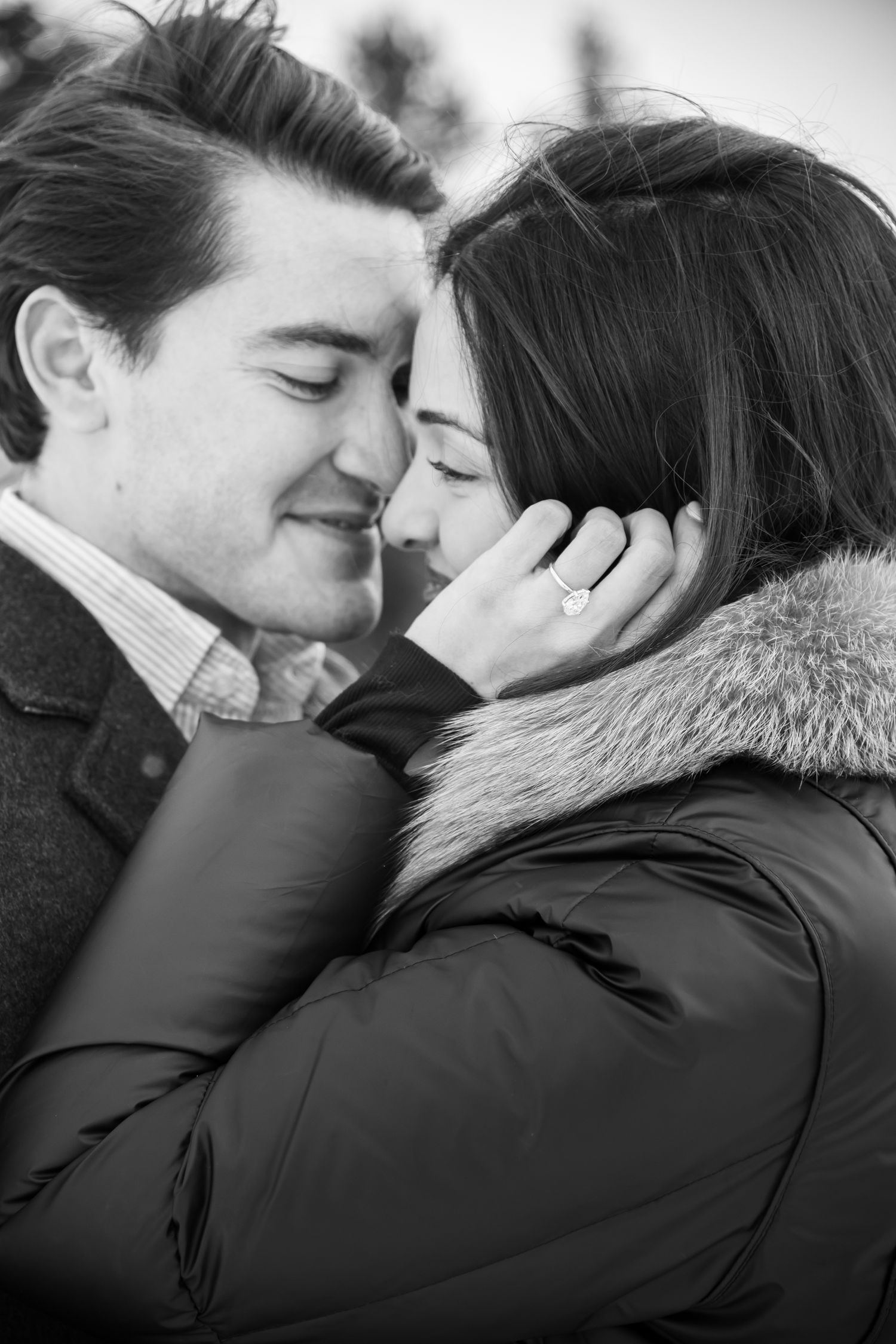 Black and white romantic photo of a couple in winter coats sharing an intimate moment with their eyes closed for Sapphire Point engagement.