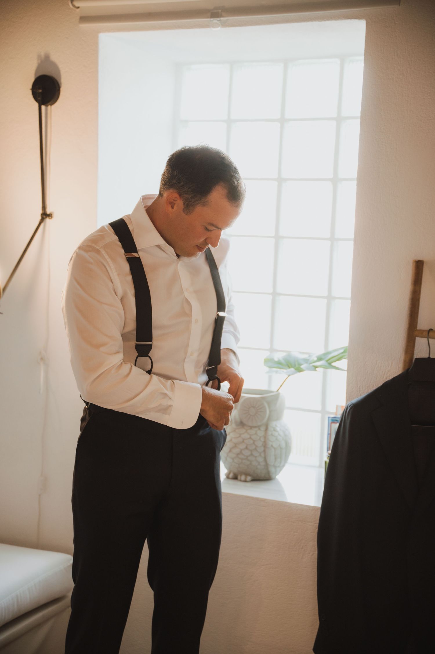 Person adjusting formal attire in front of window during wedding preparations.