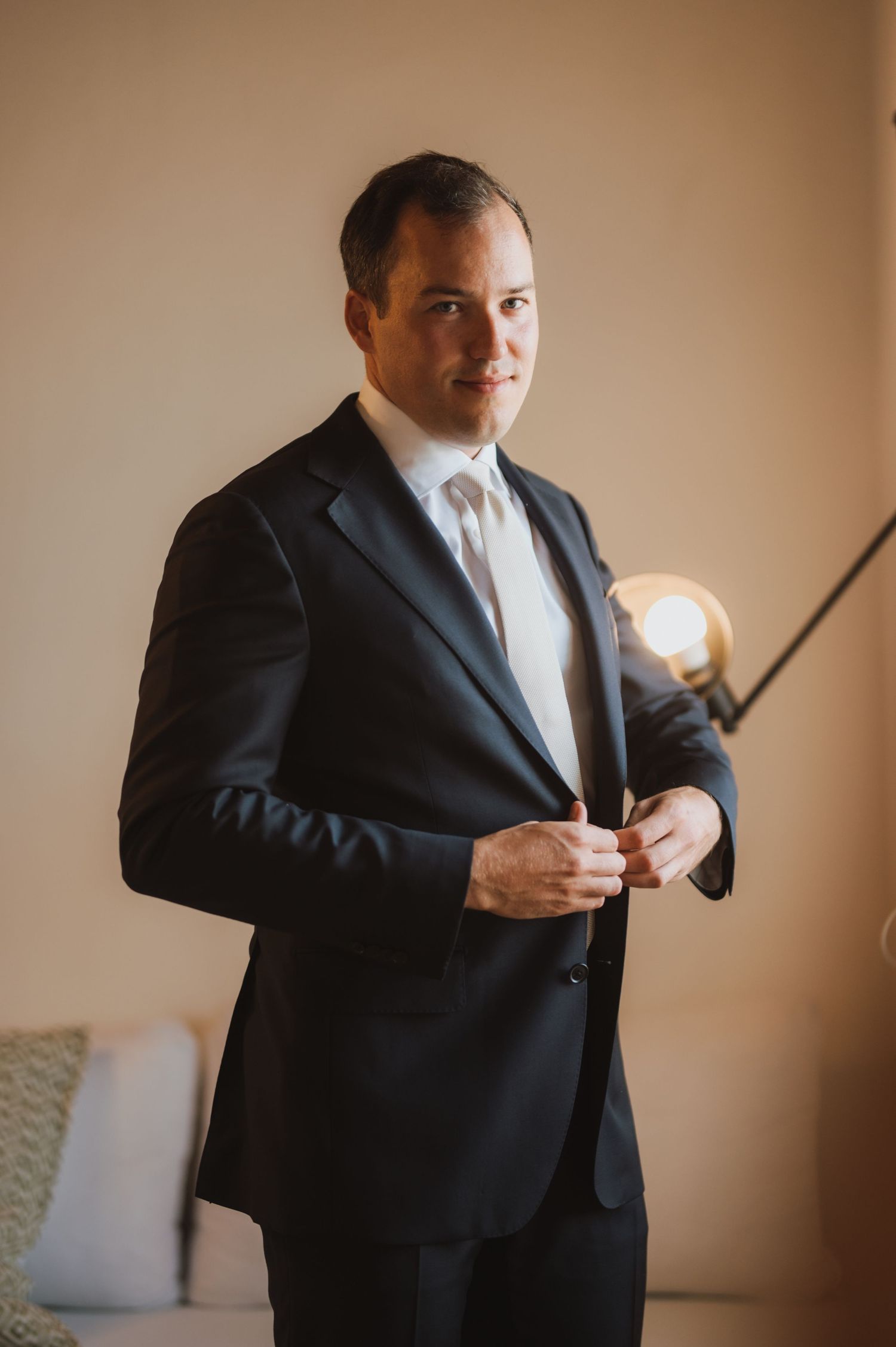Groom adjusts tie while getting ready in formal black suit.