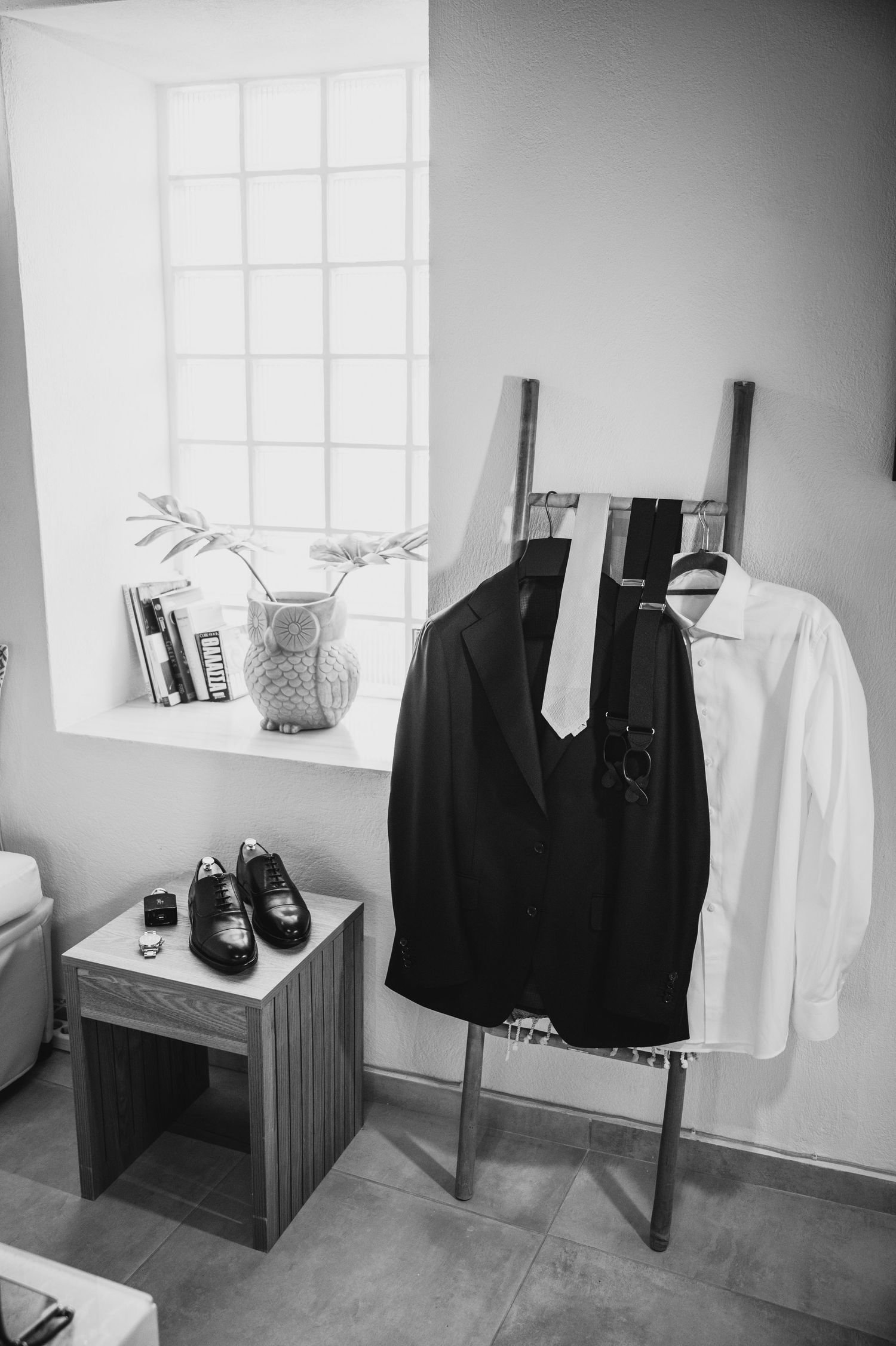 Wedding attire and formal shoes displayed in a room with a window and clothing rack.