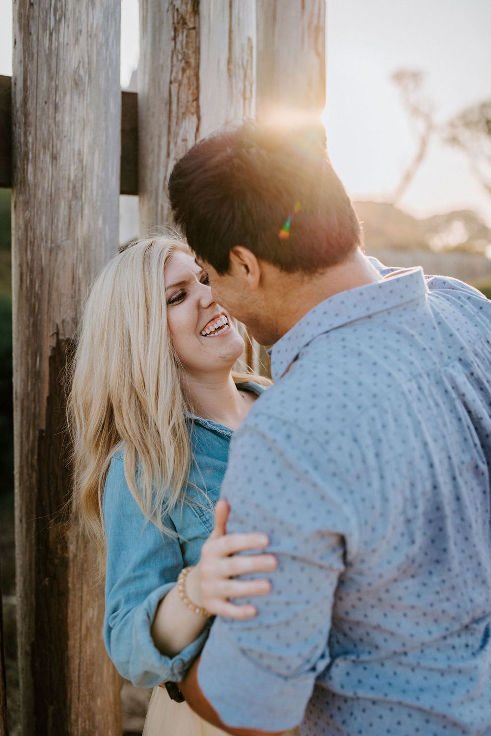 A romantic couple shares tender moments and laughter against a wooden backdrop at sunset.