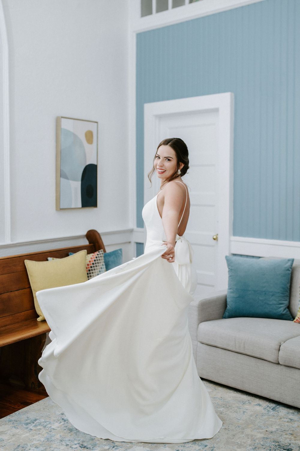 A flowing white wedding dress twirls gracefully in a blue-walled room with modern furnishings and decor.