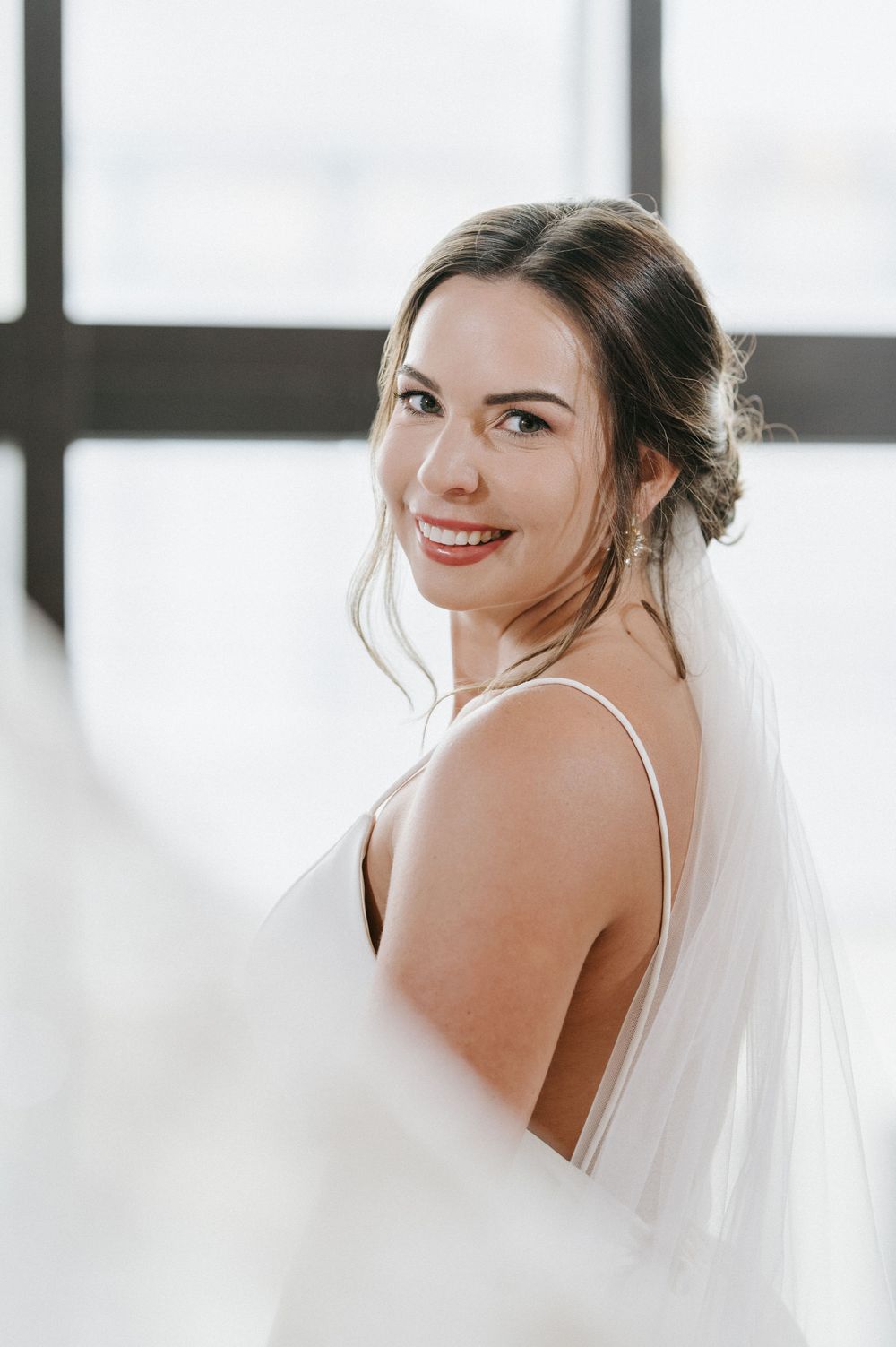 A radiant bride in a white wedding dress and veil smiles joyfully during her wedding day photoshoot.