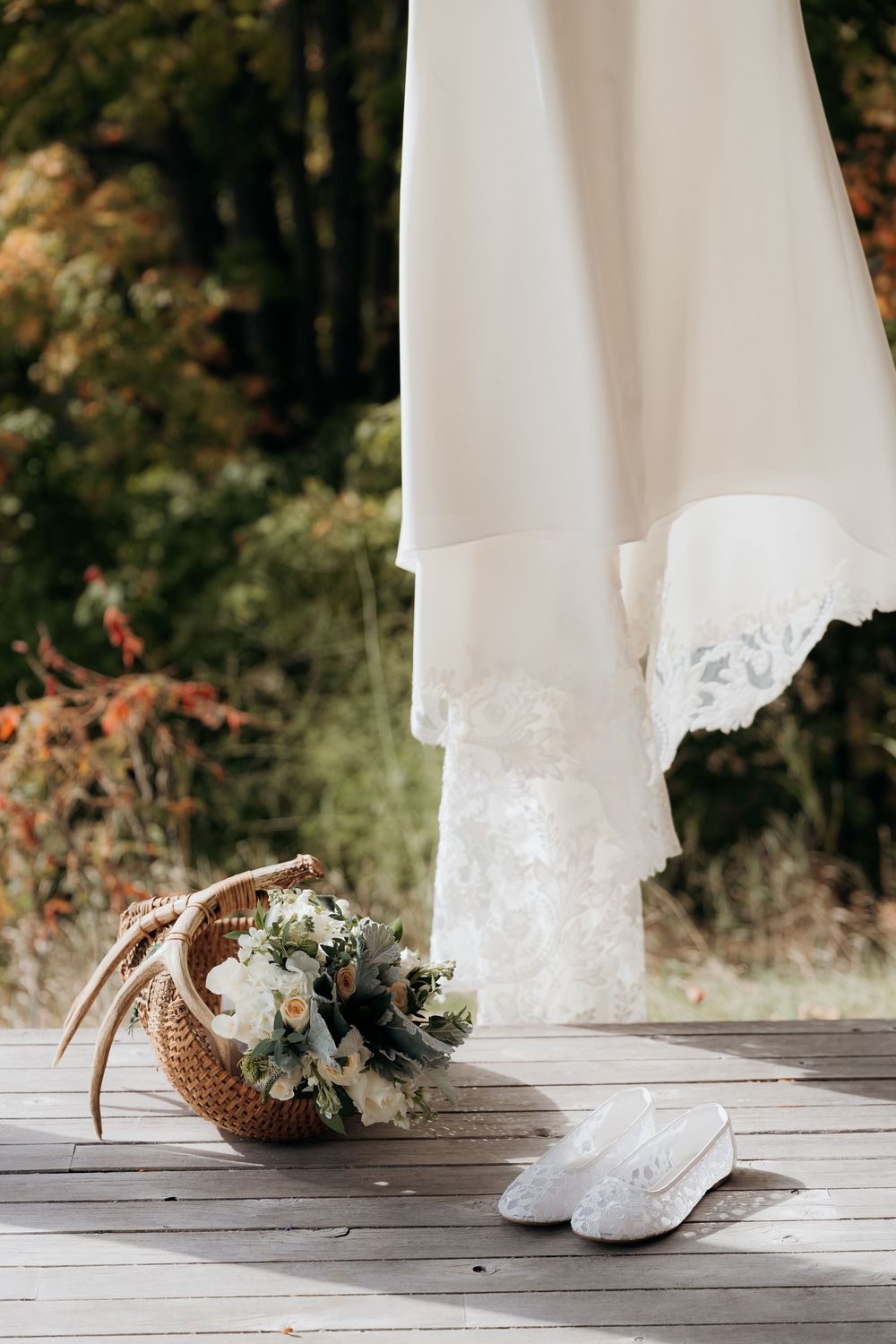 White lace wedding dress hem and bridal shoes with floral bouquet on wooden deck.