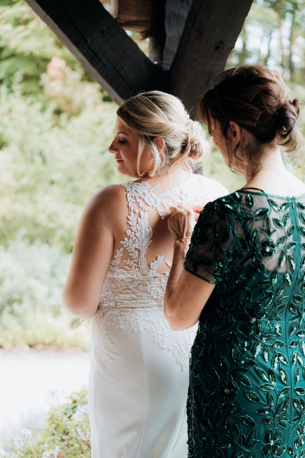 Close-up details of a white lace wedding dress next to an emerald green formal gown. Mom and Daughter first look. Wedding day in Michigan.