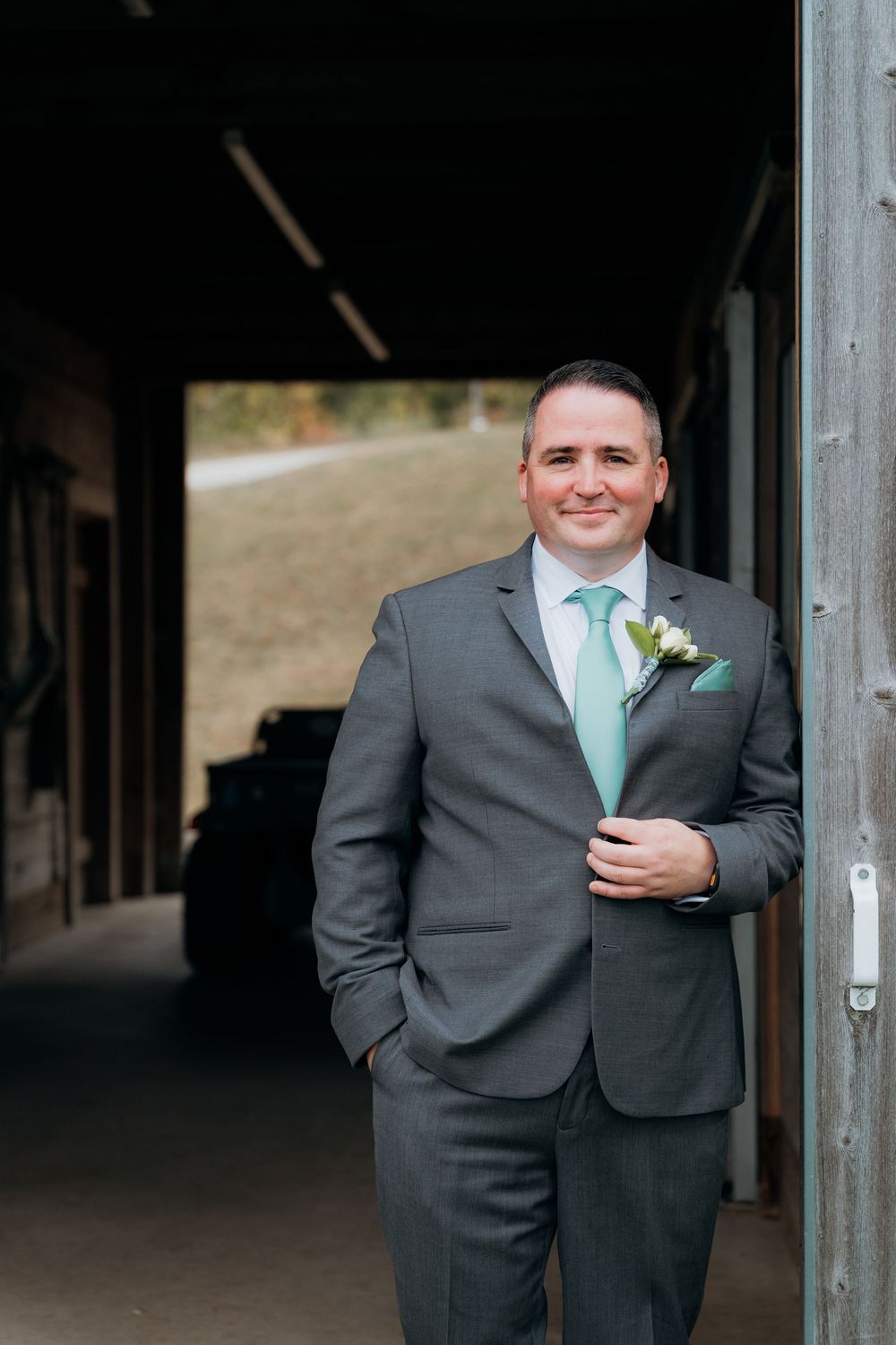 Groom in grey suit with mint tie poses in rustic barn doorway. The Garvey wedding farm in Traverse City Michigan.