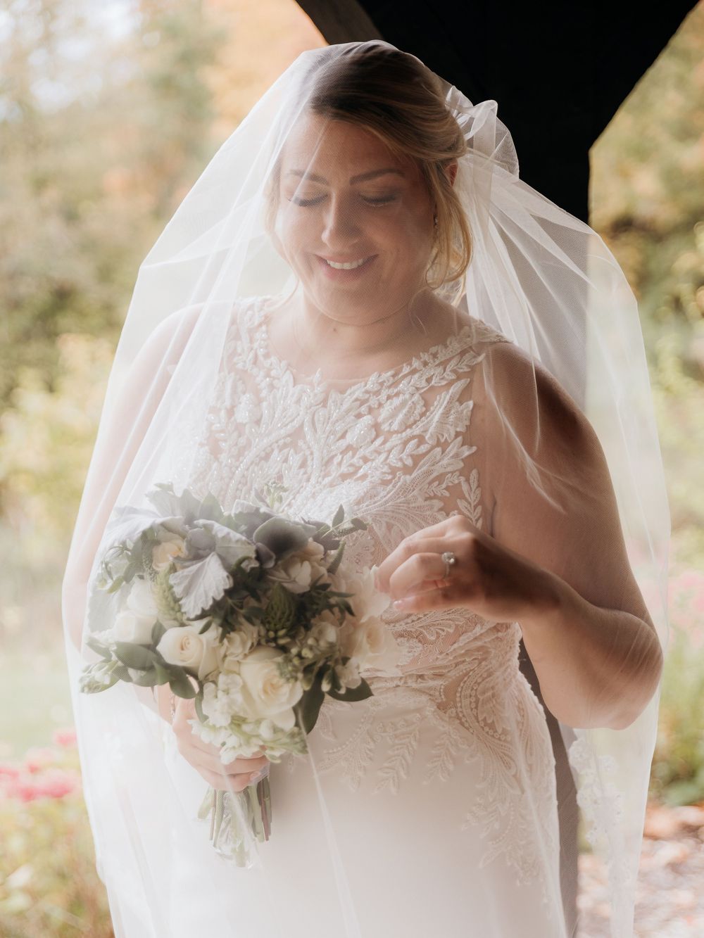 Bride holding a delicate white flower and green bouquet against her lace detailed veil. Bridal portraits. Wedding day in Traverse City MI.