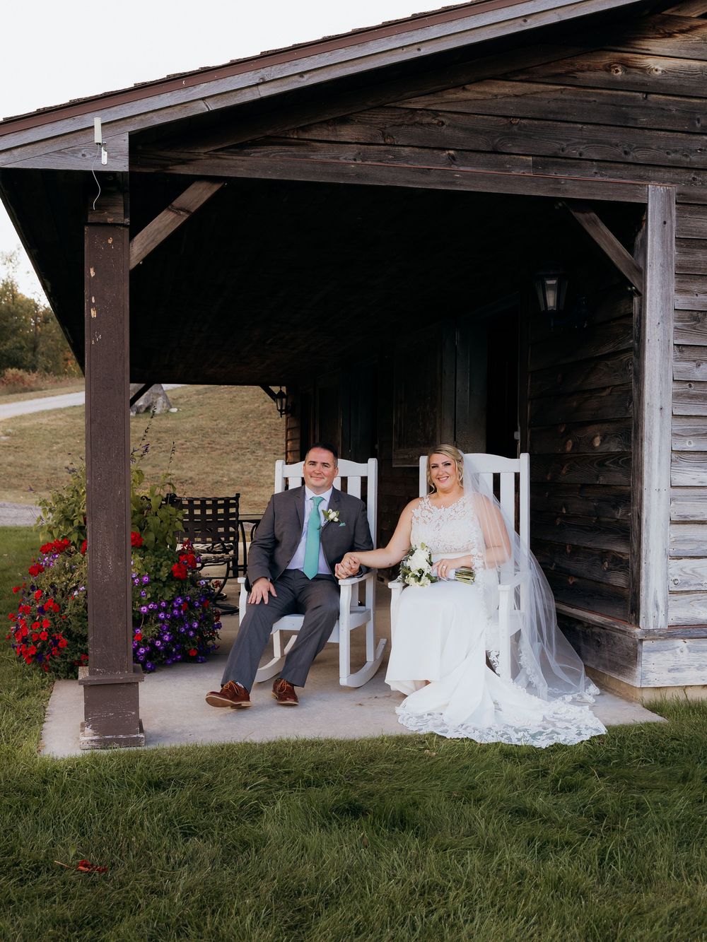 Couple sitting under a rustic wooden porch with hanging flower baskets.