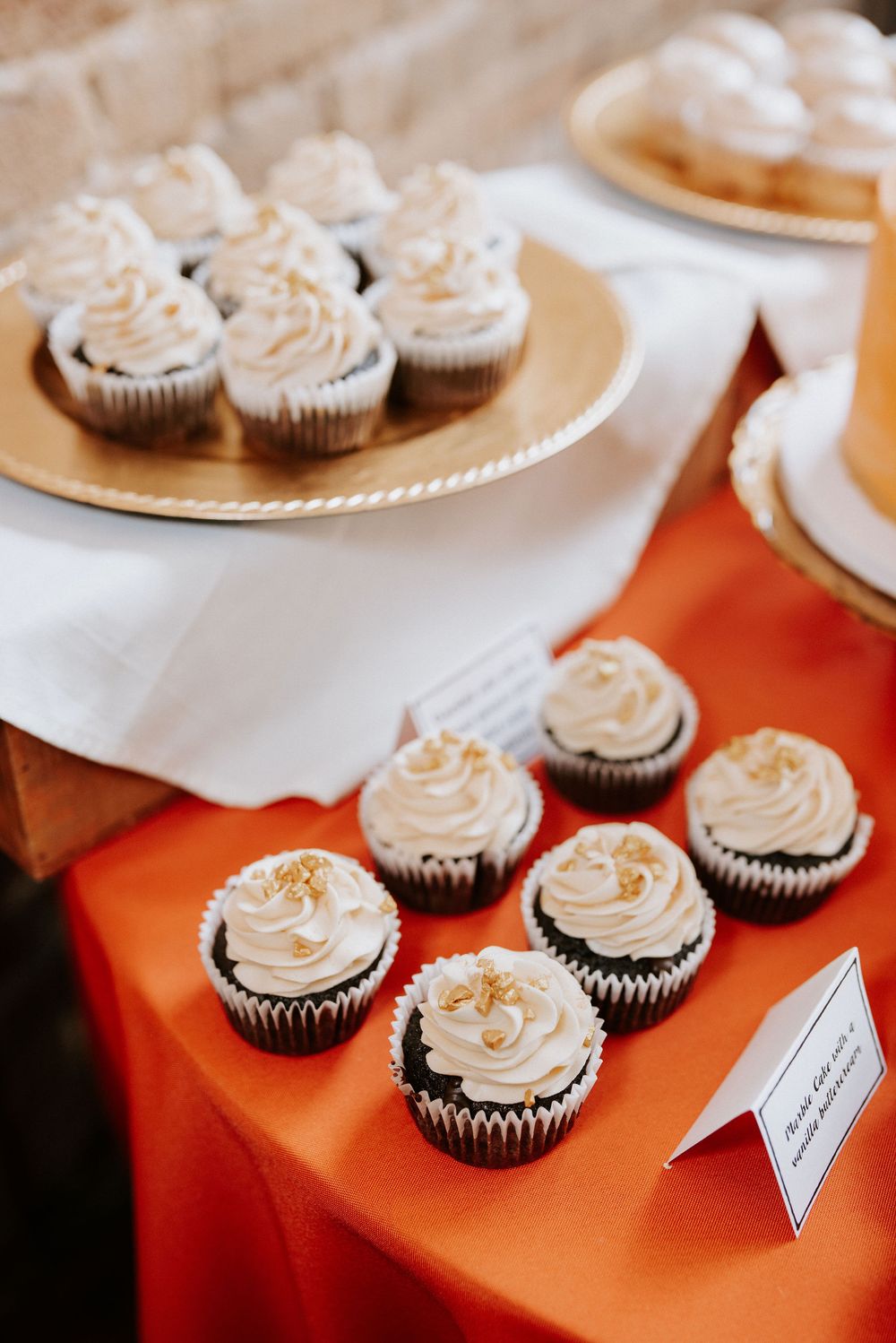 Chocolate cupcakes with swirled vanilla frosting arranged on an orange tablecloth with small name cards.