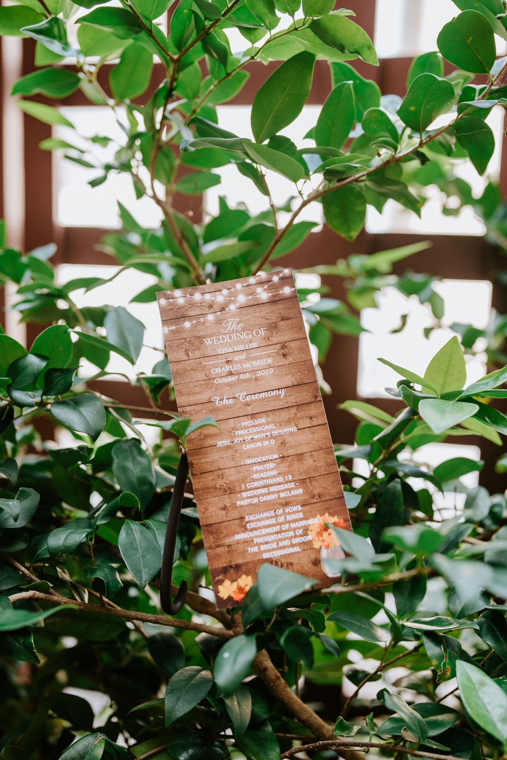 Copper-colored wedding program details displayed on circular discs nestled among green foliage.