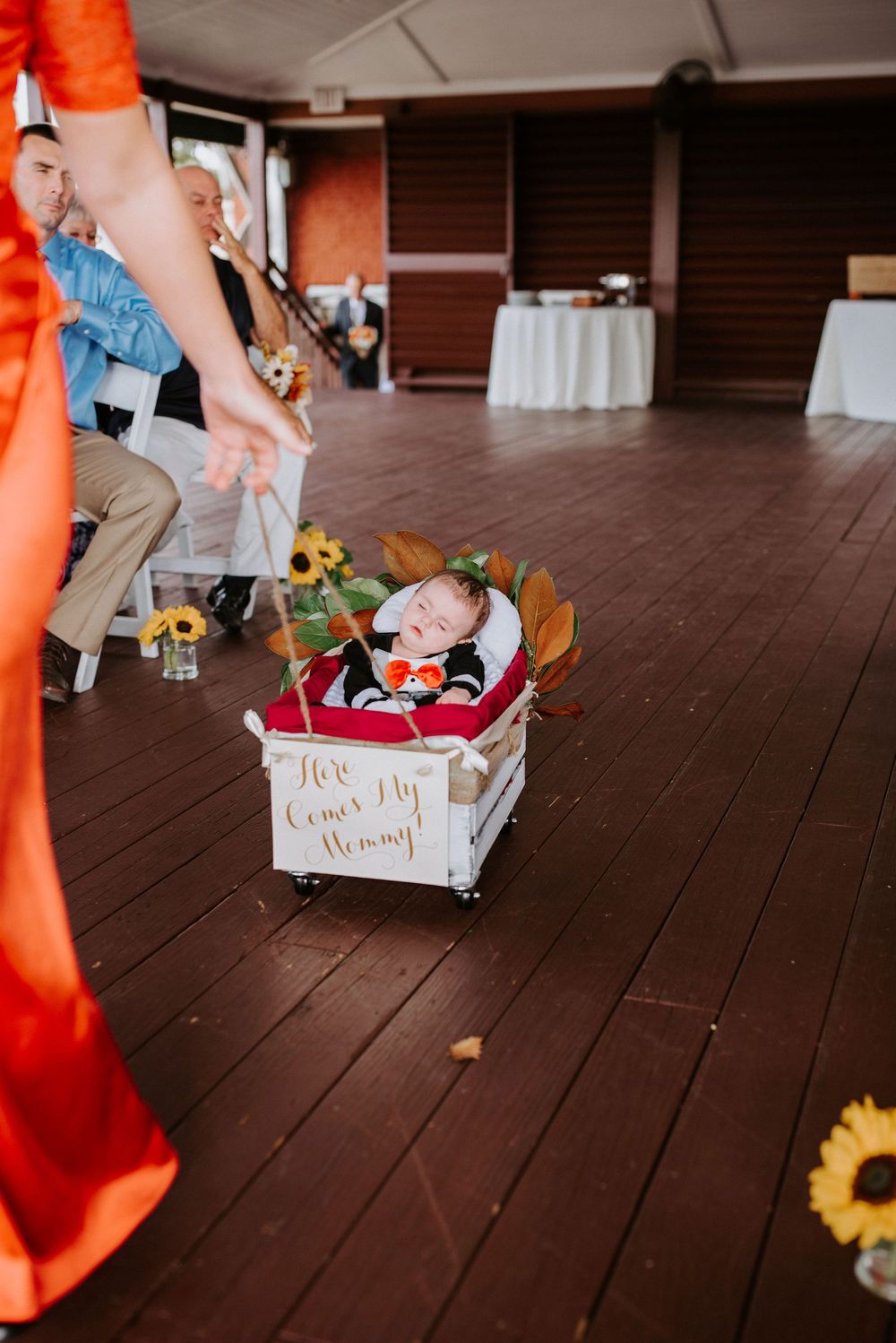 White wooden box filled with sunflowers and decorative items sits on dark hardwood floor at wedding reception.