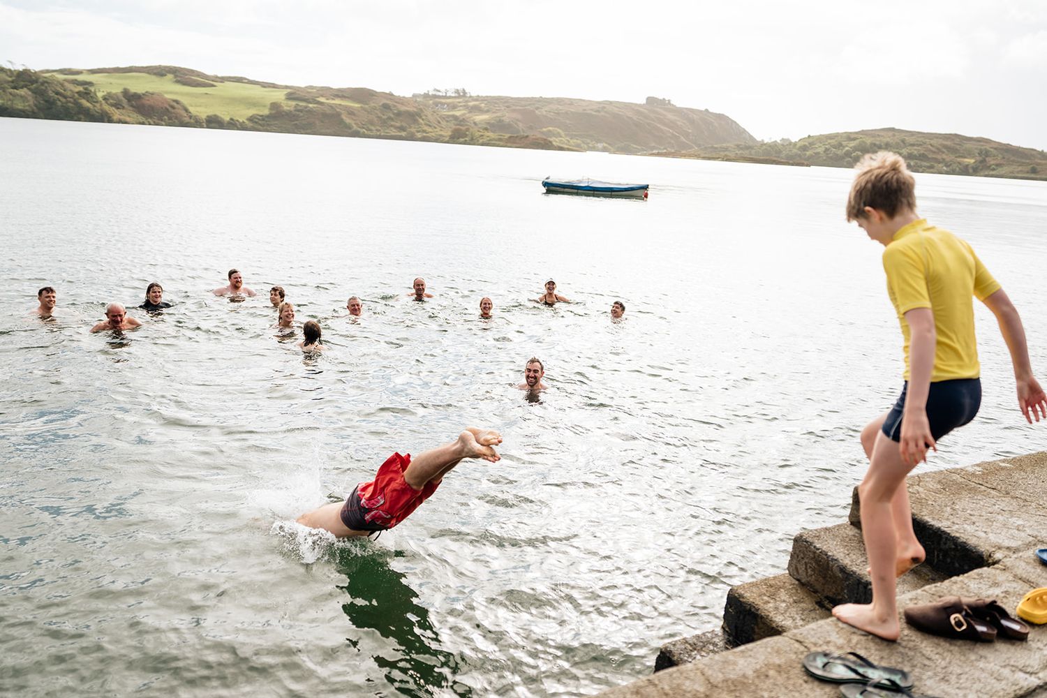A sequence of action shots showing someone diving and jumping into a lake from a rocky shoreline on a sunny day.