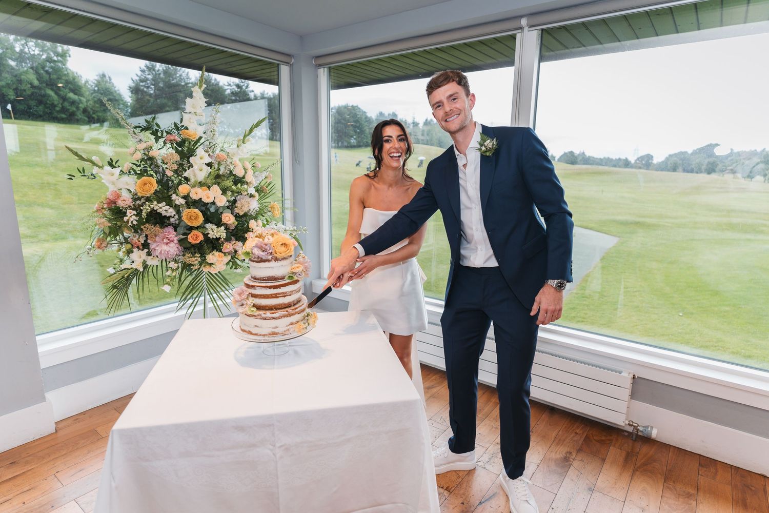 A bright sunlit porch with panoramic windows overlooking a lush green golf course and floral arrangements.