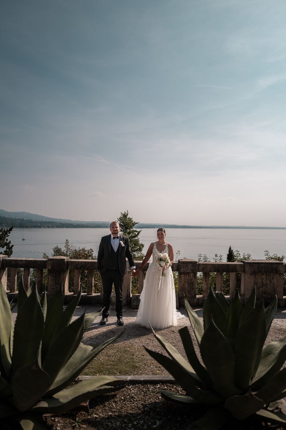Brautpaar steht zwischen Agaven auf einer Terrasse mit Blick auf den See.