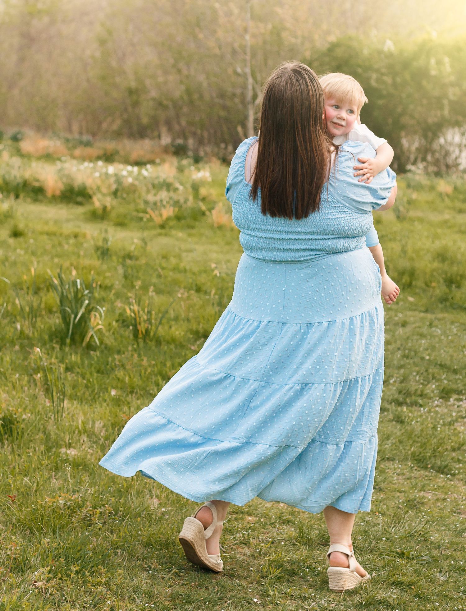 A light blue flowy dress twirls gracefully in a sunlit meadow during a golden hour photoshoot.
