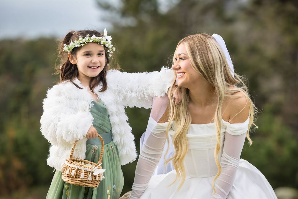 Children dressed as angels with white dresses and wings play together in a garden setting.
