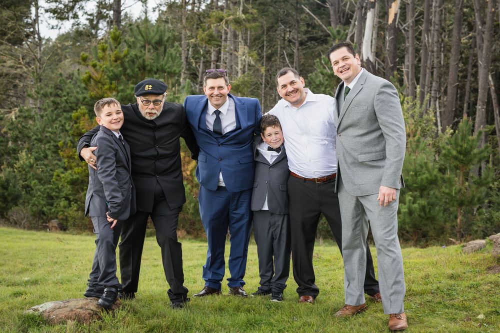 Groomsmen in suits pose playfully together in a wooded outdoor setting for wedding party photos.