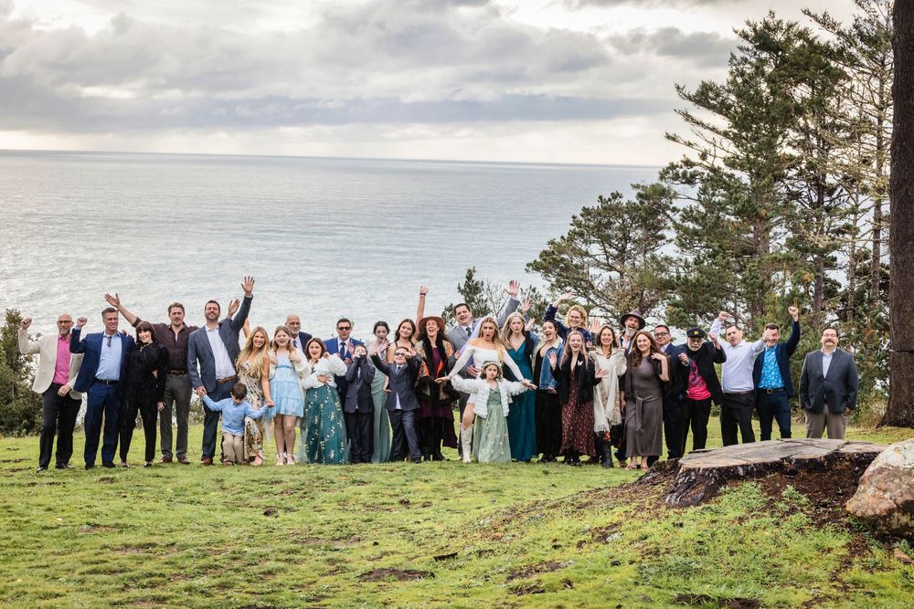 A large group of people stand together on a scenic hilltop overlooking a landscape during a gathering.