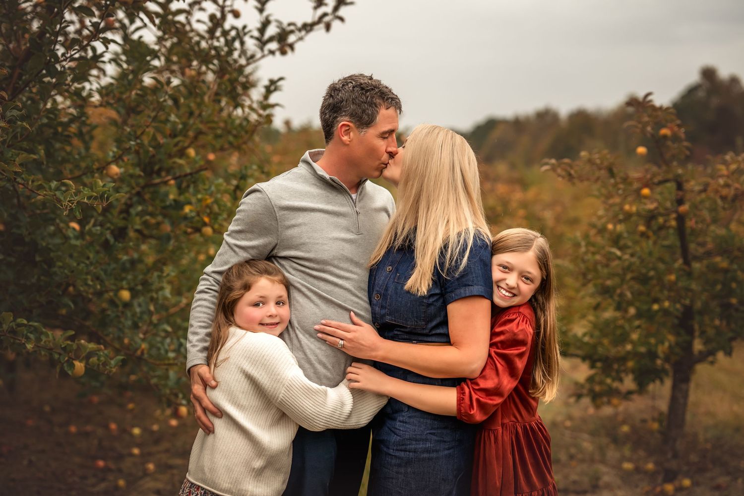 Family embraces outdoors during autumn photoshoot with fall foliage in background.